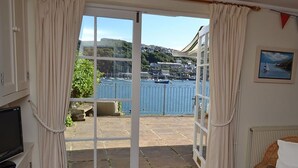 A room with a sliding glass door leading to a patio with a view of a harbor and hills. - 3 bedroom accommodation in Fowey (Fowey)