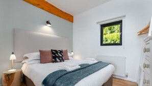 A bedroom with a bed, bedside lamps, a window with a view of greenery, and a wooden ceiling.