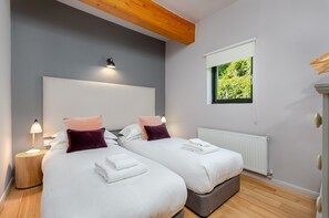 Une chambre moderne avec deux lits, une grande fenêtre donnant sur un paysage verdoyant, un plafond en bois et un radiateur blanc.