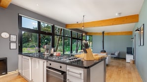 A modern kitchen with a large island, built-in oven, and a view of a garden through large windows.