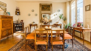 Ein Esszimmer mit einem Holztisch, Stühlen und einem gemusterten Teppich. An den Wänden befinden sich Dekorationen, ein Spiegel und ein Fenster mit Blick.