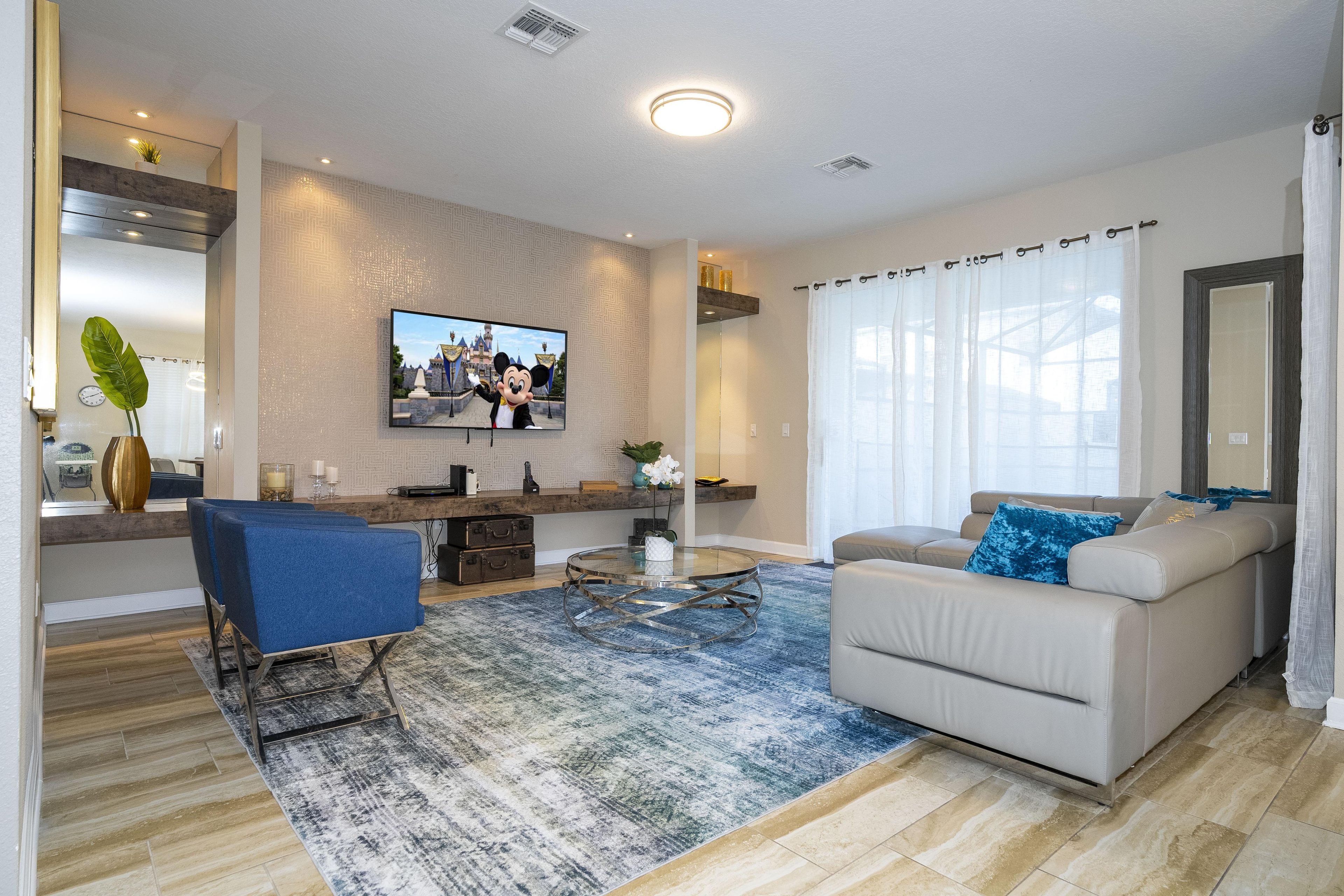 A modern living room with a flat-screen TV, a sofa, a coffee table, and a patterned rug.