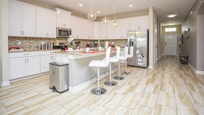 A modern kitchen with white cabinets, a central island with bar stools, stainless steel appliances, and a tiled floor. - 4764- Great Family Home near Disney, Pool & Spa - Storey Lake Resort (Kissimmee)