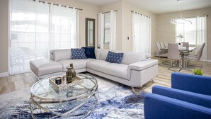 A modern living room with a sectional sofa, a glass coffee table, and a dining area with a table and chairs. - 4764- Great Family Home near Disney, Pool & Spa - Storey Lake Resort (Kissimmee)