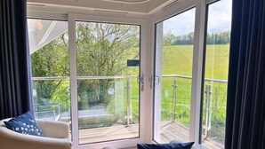 Una habitación con una puerta corrediza de vidrio que da a una terraza con vistas a un paisaje verde.