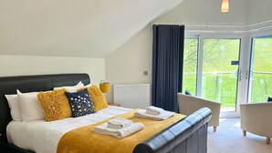Una habitación de hotel moderna con una cama grande, un balcón y vistas a zonas verdes.
