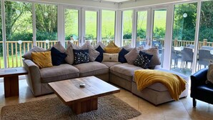 Una sala de estar moderna con un sofá seccional, una mesa de centro de madera y vistas a un jardín exuberante a través de grandes ventanales.