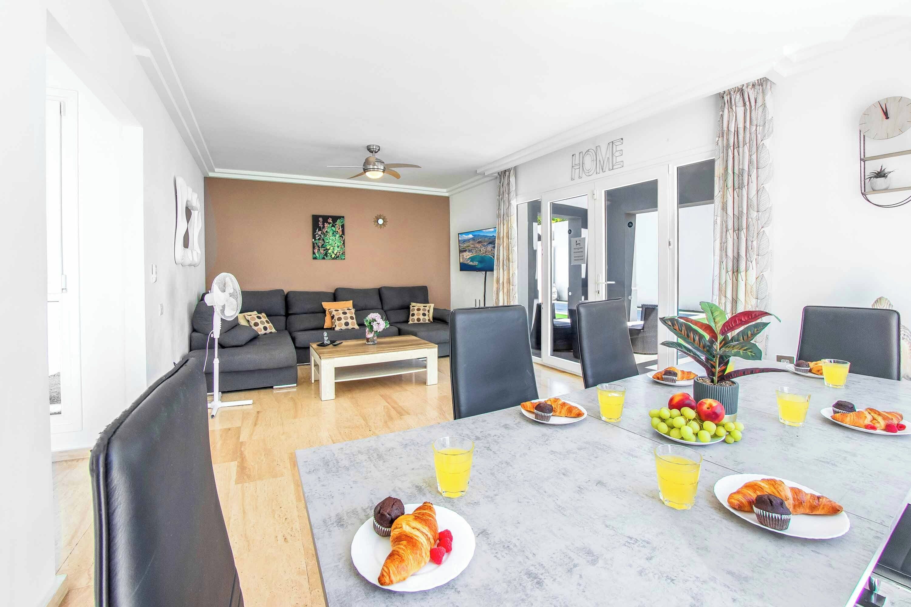 A dining area with a table set for breakfast, including croissants, muffins, and fruit.