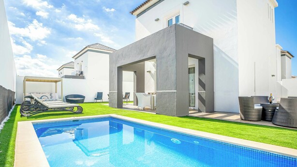 Ein moderner Poolbereich mit einem klaren, blauen Pool, einer grünen Rasenfläche und einer Terrasse mit Gartenmöbeln.