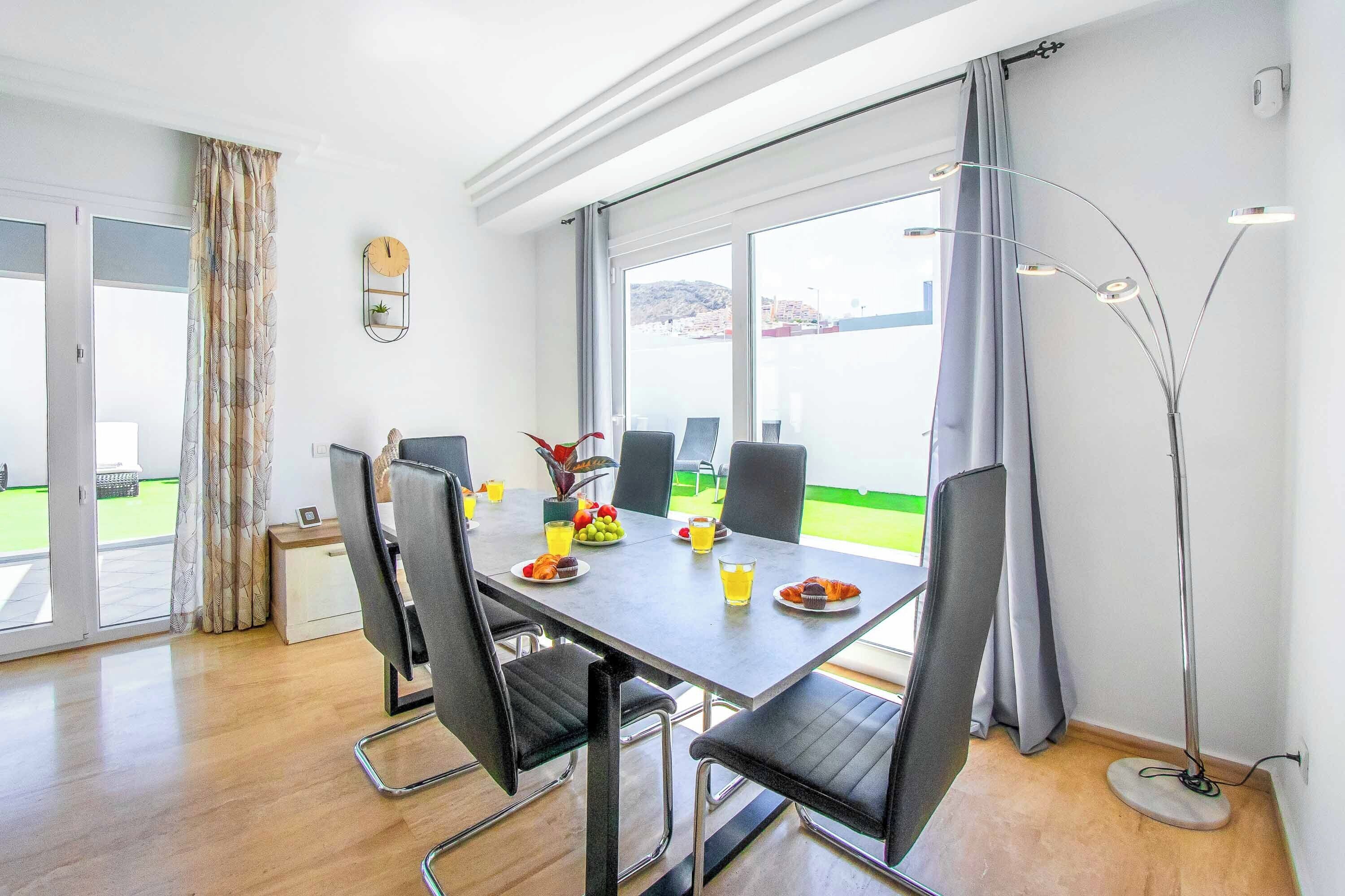 Un coin repas avec une table dressée pour quatre personnes, un lampadaire au design moderne et une vue sur l’extérieur.