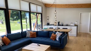 A modern living room with a sectional sofa, a wooden coffee table, and a view of the garden through large windows.