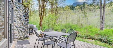 A wooden deck with a stone wall, outdoor table and chairs, and a view of a forested area.