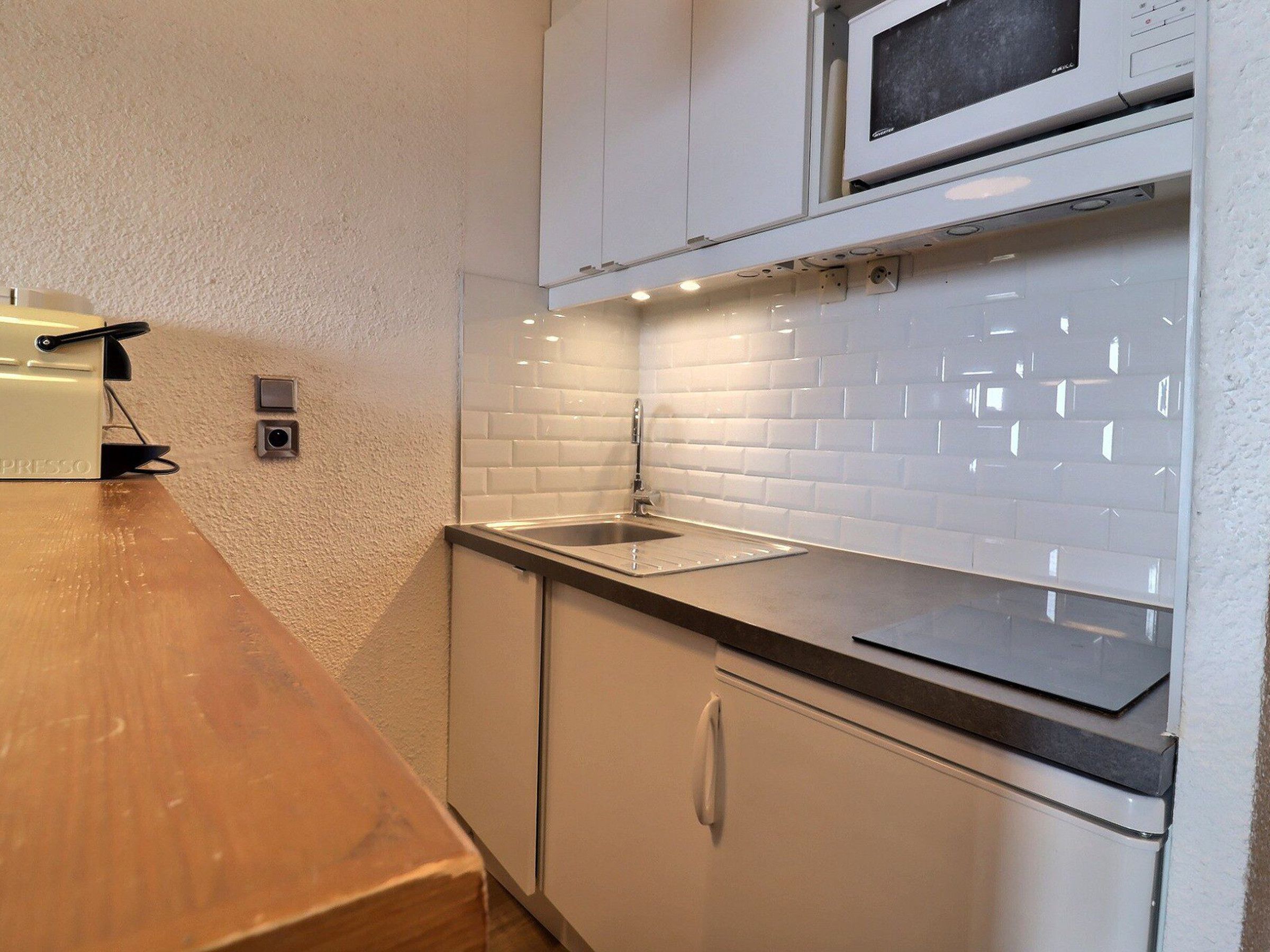Cucina con mobili bianchi, piano di lavoro in legno, forno a microonde integrato e lavello.