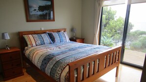 Une chambre à coucher avec un lit en bois, deux tables de chevet, une commode, une fenêtre donnant sur un paysage verdoyant et un tableau encadré au mur.