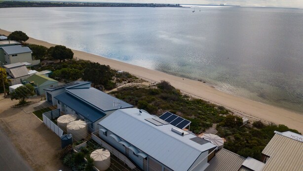 Une propriété située en bord de mer, offrant une vue sur la plage, dotée de panneaux solaires et d’un grand réservoir d’eau.