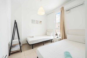 Una habitación de hotel con dos camas, una lámpara de pie, una ventana con cortinas y un aire acondicionado instalado en la pared.