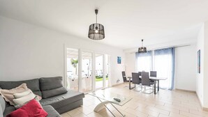 Una sala moderna con un sofá gris, una mesa de centro de vidrio y un comedor con una mesa y sillas.
