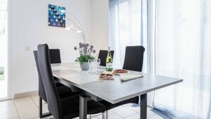 Een eetgedeelte met een tafel, stoelen, een vaas met bloemen, een fles en een bord eten.