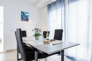 Un comedor con una mesa, sillas, un florero con flores, una botella y un plato de comida.