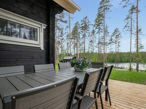 A wooden deck with a table and chairs, overlooking a lake and forest.
