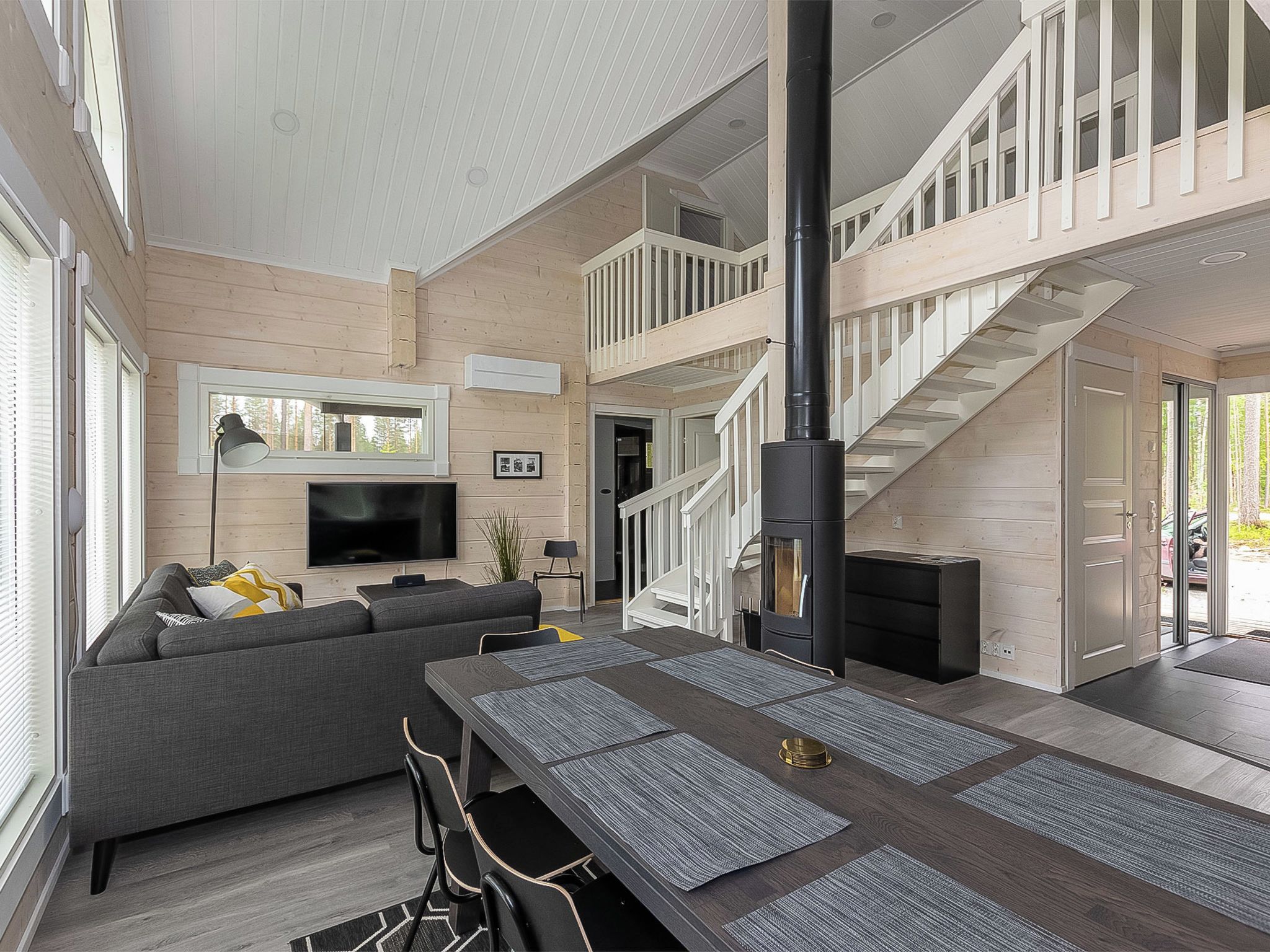 A spacious living area with a modern fireplace, a staircase leading to an upper level, and a flat-screen TV mounted on the wall.