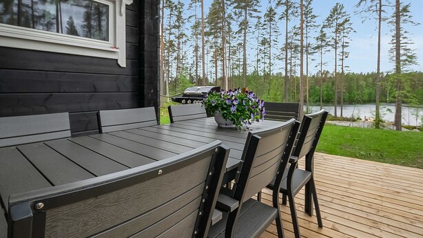 Eine Holzterrasse mit Tisch und Stühlen mit Blick auf einen See und hohe Bäume.