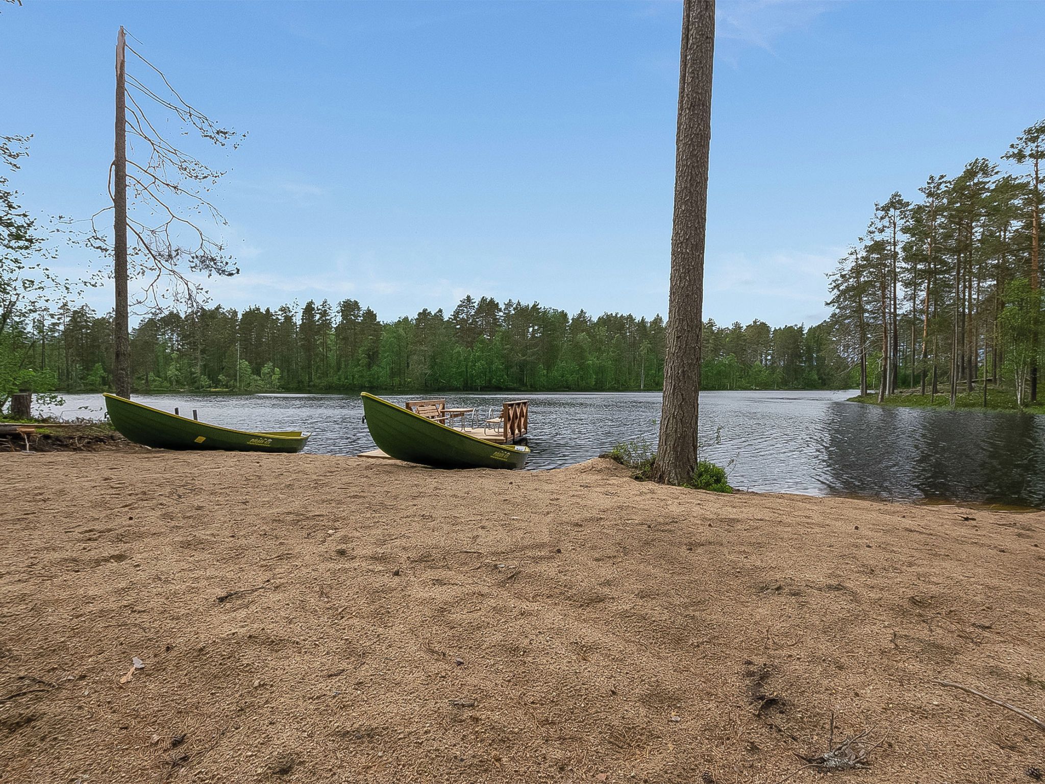 A lakeside setting with two green boats on a sandy shore, surrounded by a forest.