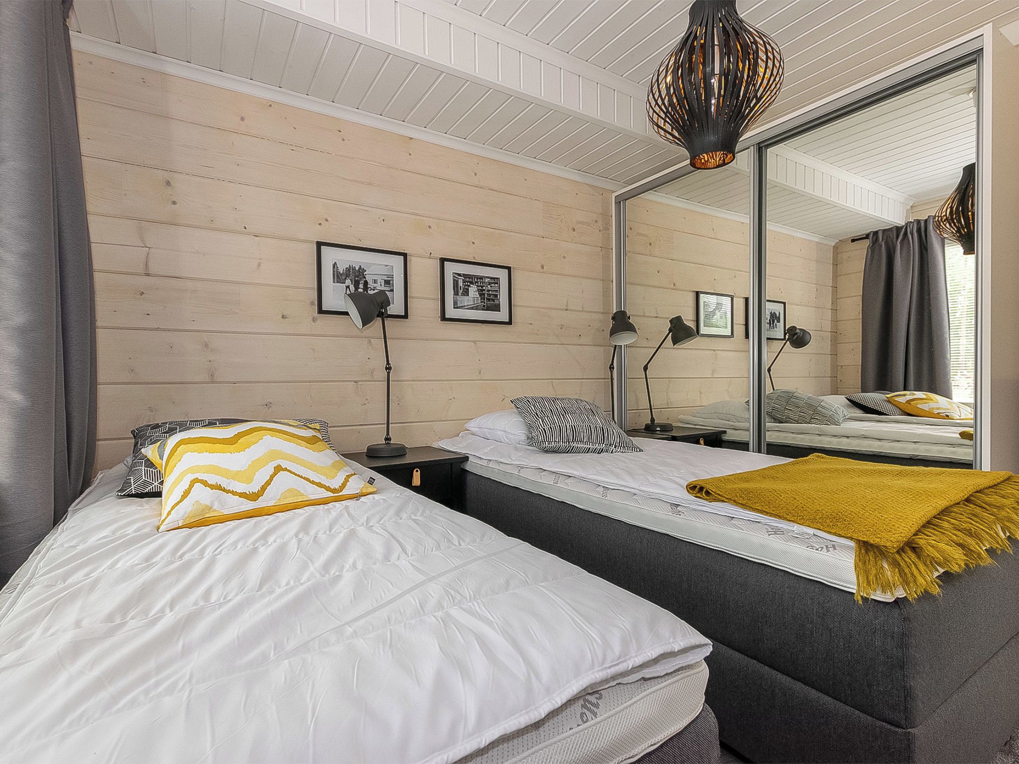 Une chambre avec deux lits, un grand miroir et deux lampes fixées au mur.