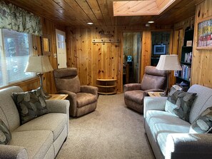 Relax in a warm and inviting space with comfortable seating, a bookshelf, and a window with blinds.