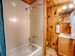 Bathroom features a bathtub with a wall-mounted showerhead, a wooden cabinet, and a mirror.