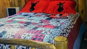 A wooden-paneled room with a bed featuring a red and black patterned quilt, two pillows with deer head designs, and a wall sign that reads "blessed."