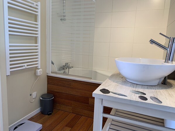 A bathroom with a white bathtub, a large white sink, a shower, and a wooden floor.