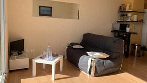 A living room with a dark grey sofa, a white coffee table, and a small white side table. There is a framed picture on the wall and a kitchen area with a microwave and coffee maker. - Duplex T2 Arcachon: Terrasse, Wifi, 100m Plage, Proche Centre (Arcachon)