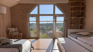 A bedroom with two beds, a chair, and a large window with a view of a town. - Duplex T2 Arcachon: Terrasse, Wifi, 100m Plage, Proche Centre (Arcachon)