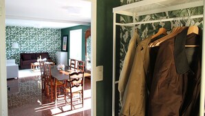 Une pièce comprenant un coin repas, un porte-manteau avec des vêtements suspendus et un mur orné d’un motif végétal.