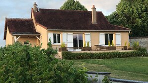Une maison à deux étages avec une grande pelouse à l’avant, une terrasse et un jardin.