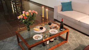 Une table basse avec un plateau en verre, agrémentée d’un arrangement floral, de bougies et d’une bouteille de vin.