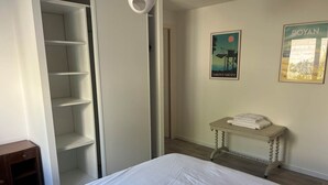 A bedroom with a bed, a wardrobe, a small table with towels, and two framed pictures on the wall.
