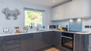 A modern kitchen with grey cabinets, a built-in oven, a microwave, and a toaster. - 2 bedroom accommodation in Fowey (Fowey)