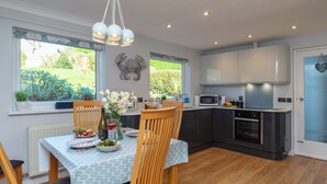 A modern kitchen with a dining area, featuring a wooden table, chairs, and a view of the garden through large windows. - 2 bedroom accommodation in Fowey (Fowey)