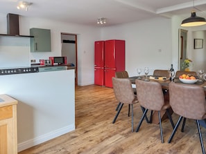 A modern kitchen with a microwave, toaster, and red refrigerator. There is a dining area with a table set for two, featuring a bowl of fruit and wine glasses.
