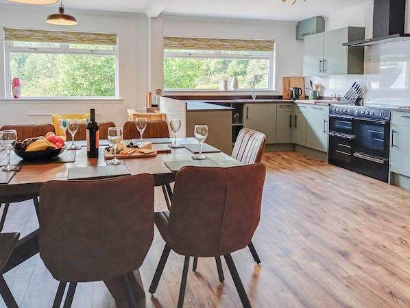 A modern kitchen with a dining area, wooden flooring, and large windows.