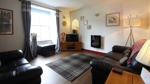 A living room with a sofa, a television, a lamp, and a window with curtains. - The Wee Nook, Birnam & Dunkeld (Birnam)