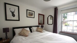 A neatly made bed with white linens and patterned pillows, a framed deer head artwork, a framed landscape painting, and a mirror on the wall. - The Wee Nook, Birnam & Dunkeld (Birnam)