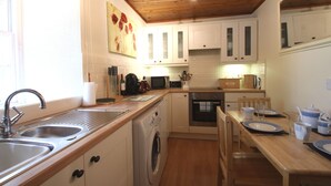 A compact kitchen with a washing machine, a microwave, and a dining area with a table set for two. - The Wee Nook, Birnam & Dunkeld (Birnam)