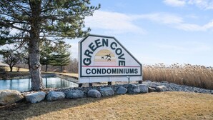 A sign for Green Cove Condominiums with a lake and trees in the background.