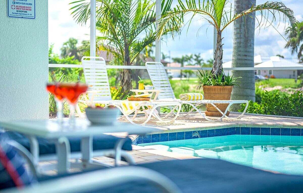 Un espace aménagé au bord de la piscine, avec des chaises longues, une table sur laquelle sont posées des boissons et des plantes en pot.