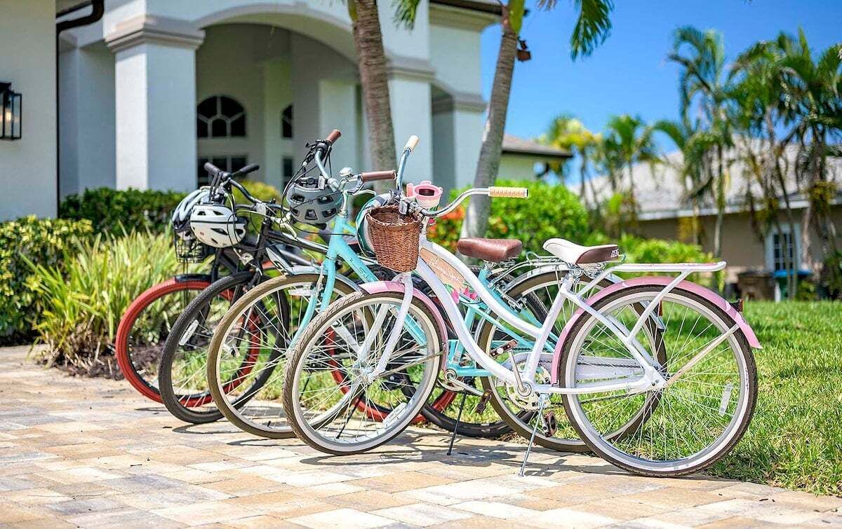 A row of bicycles parked on a paved walkway in front of a building with a white facade and columns.