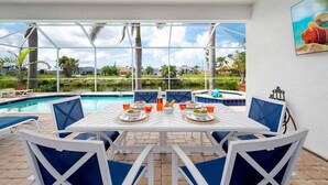 Ein Essbereich am Pool mit einem Tisch für vier Personen, umgeben von Stühlen, mit Blick auf einen Swimmingpool und Grünflächen.