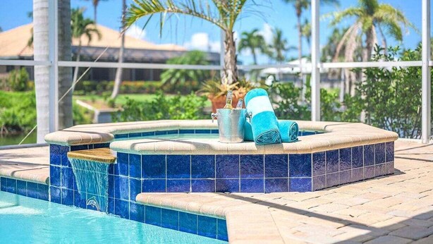 Ein Whirlpool mit blauen Fliesen, ein Eimer und ein Handtuch, vor einer Kulisse aus Palmen und blauem Himmel.